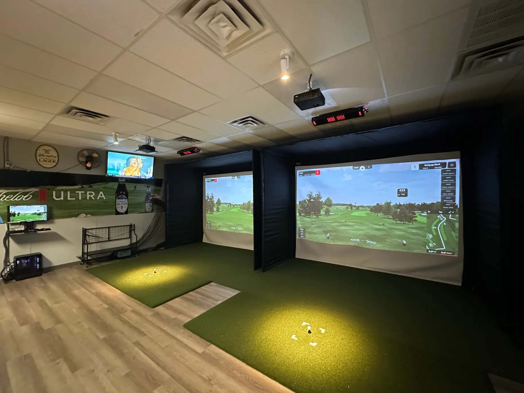 A modern golf simulator room with two large projection screens, a putting green, and a TV displaying sports, featuring a casual atmosphere A modern golf simulator room with two large projection screens, a putting green, and a TV displaying sports, featuring a casual atmosphere