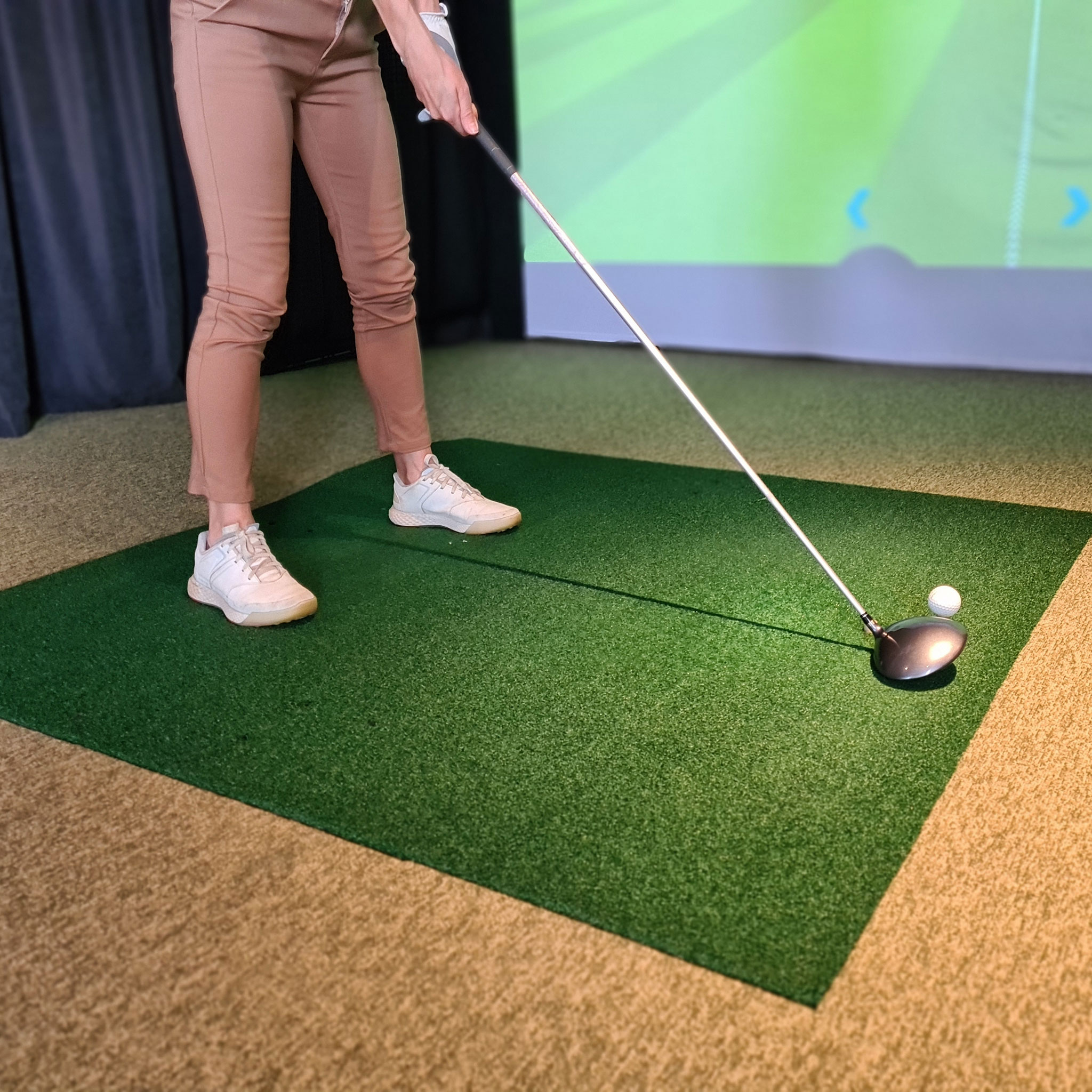 Girl golf player plays golf indoors. Golf driving range with simulator screen Girl golf player plays golf indoors. Golf driving range with simulator screen