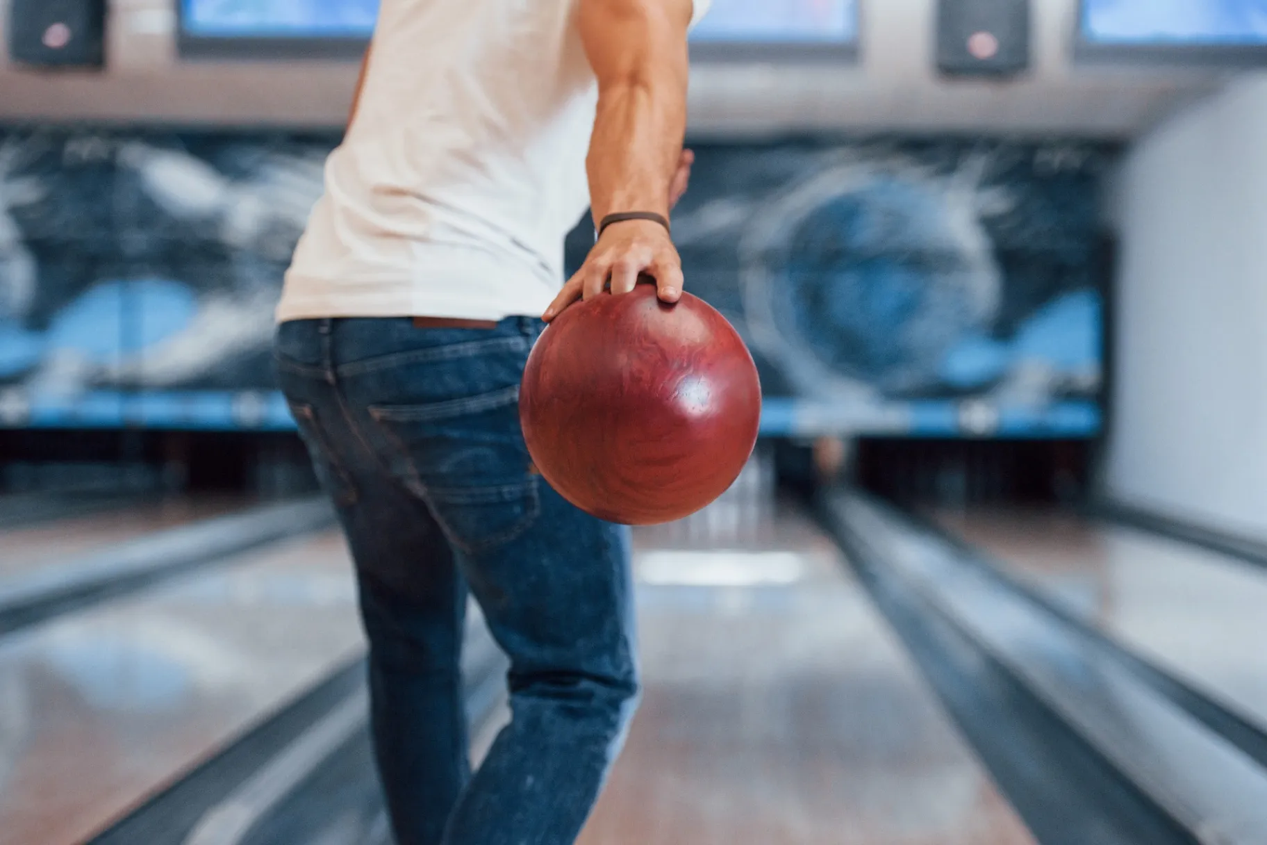 Rear particle view of man in casual clothes playing bowling in the club Rear particle view of man in casual clothes playing bowling in the club